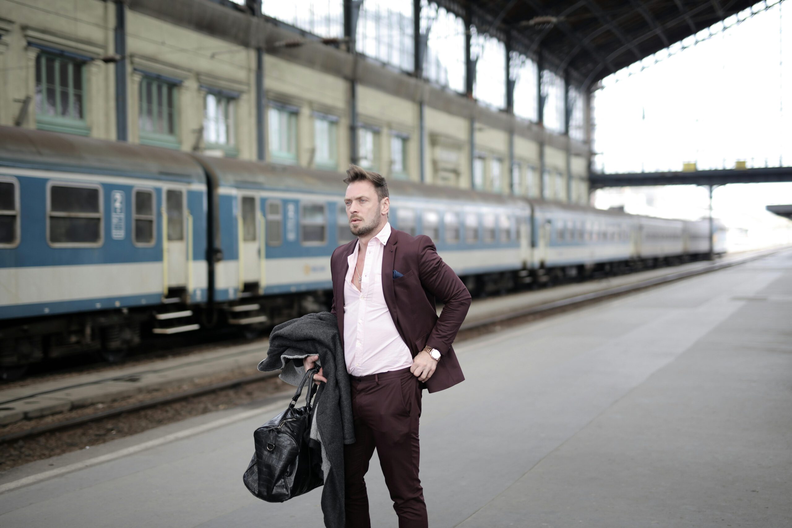 Elegant businessman standing on platform and waiting for train on railway station